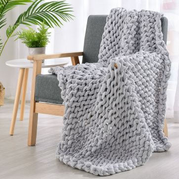 Grey hand knitted weighted blanket draped over chair.